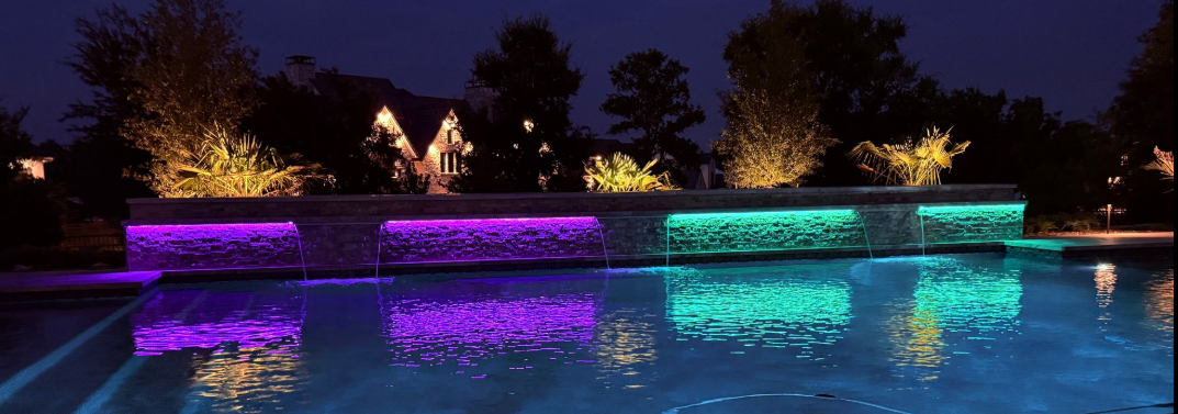 Color-changing LED lighting illuminating a pool water feature wall creating vibrant nighttime outdoor lighting effects