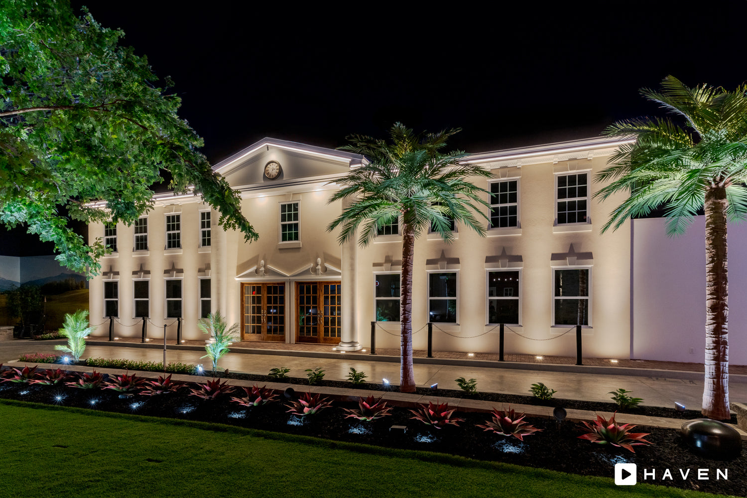 Commercial landscape lighting illuminating a showroom building with palm trees, architectural uplighting, and pathway lighting at night.