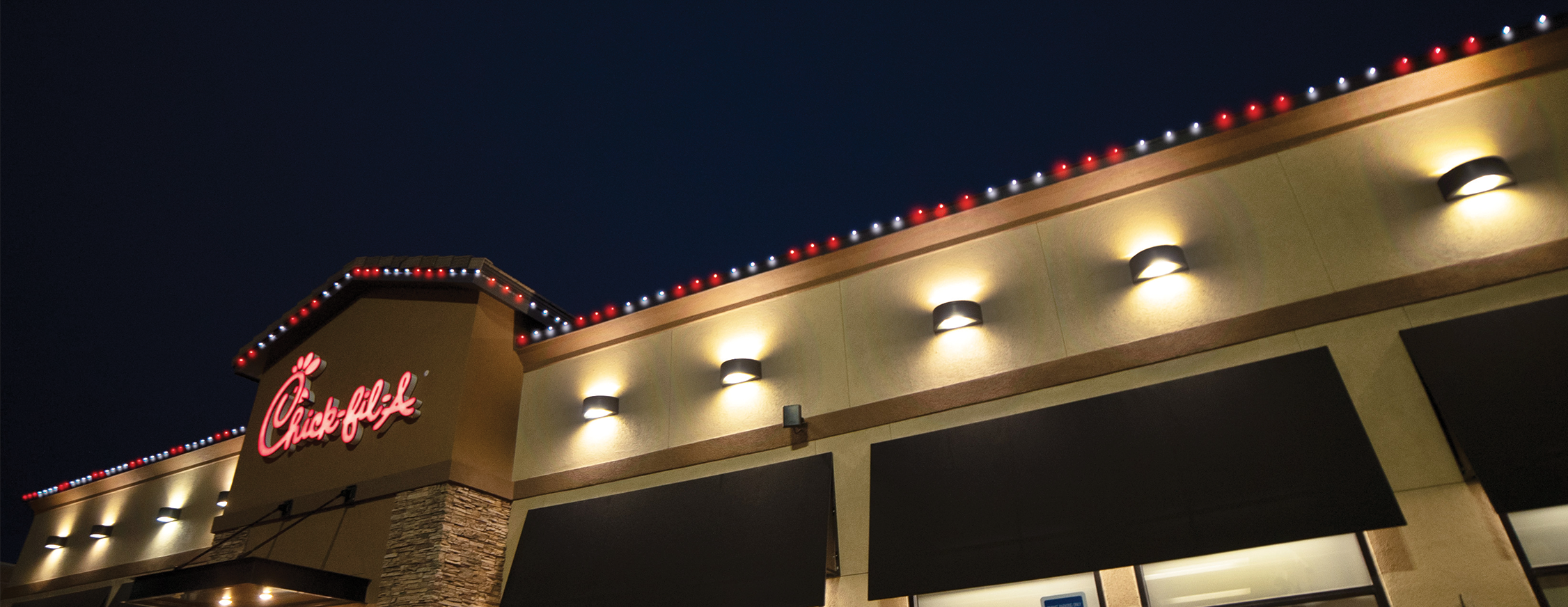 Permanent roofline lighting installed on a Chick-fil-A restaurant with red and white LED lighting along the roofline at night.