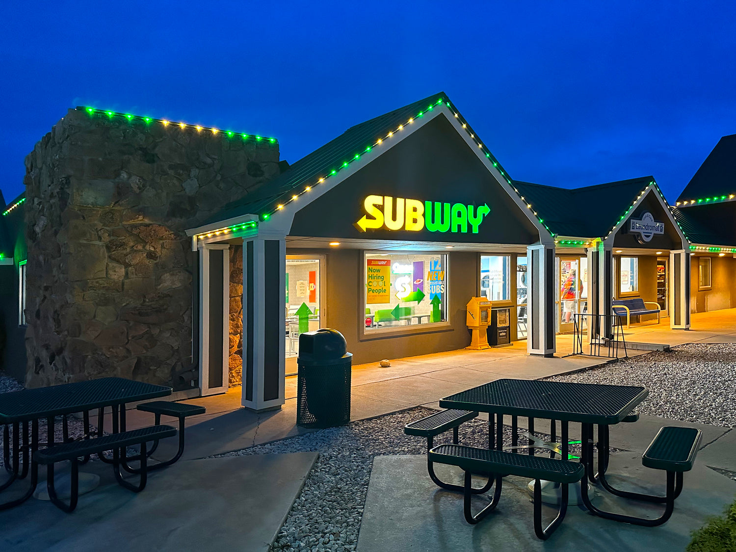 Green and warm white commercial roofline lighting installed on a Subway restaurant building at dusk.