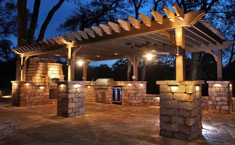 Hardscape and landscape lighting illuminating stone outdoor kitchen and outdoor living space
