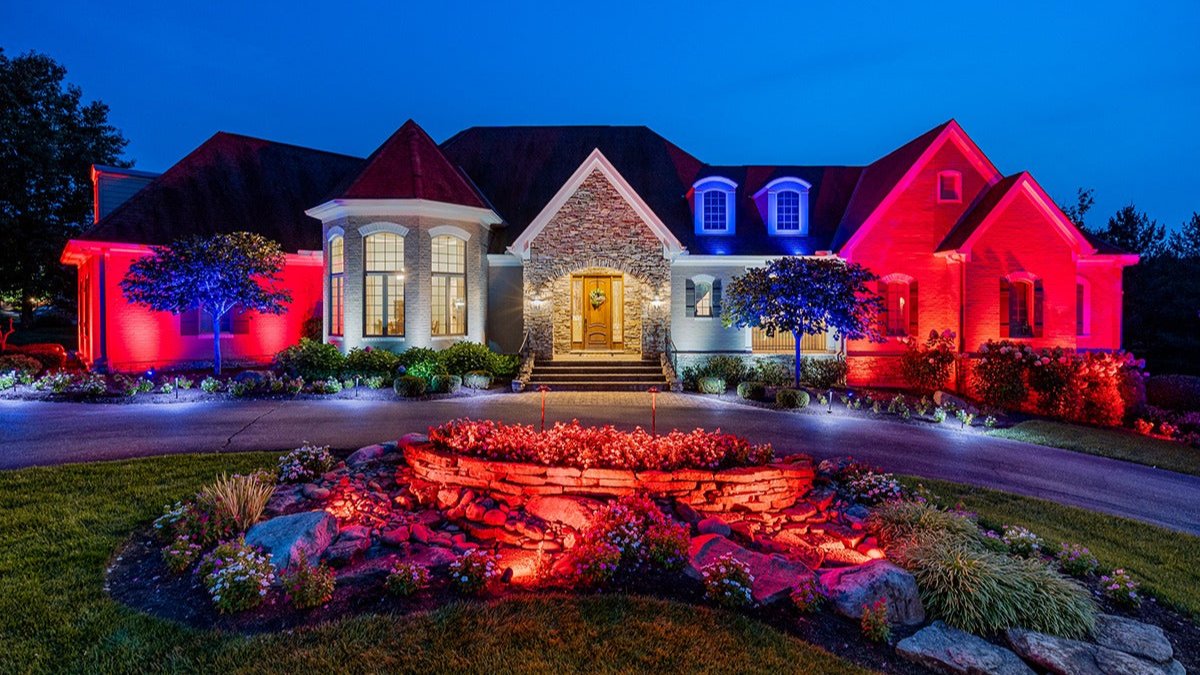 Color-changing outdoor lighting on luxury home in The Villages Florida featuring red, white, and blue landscape lighting, architectural lighting, and illuminated front yard stonework