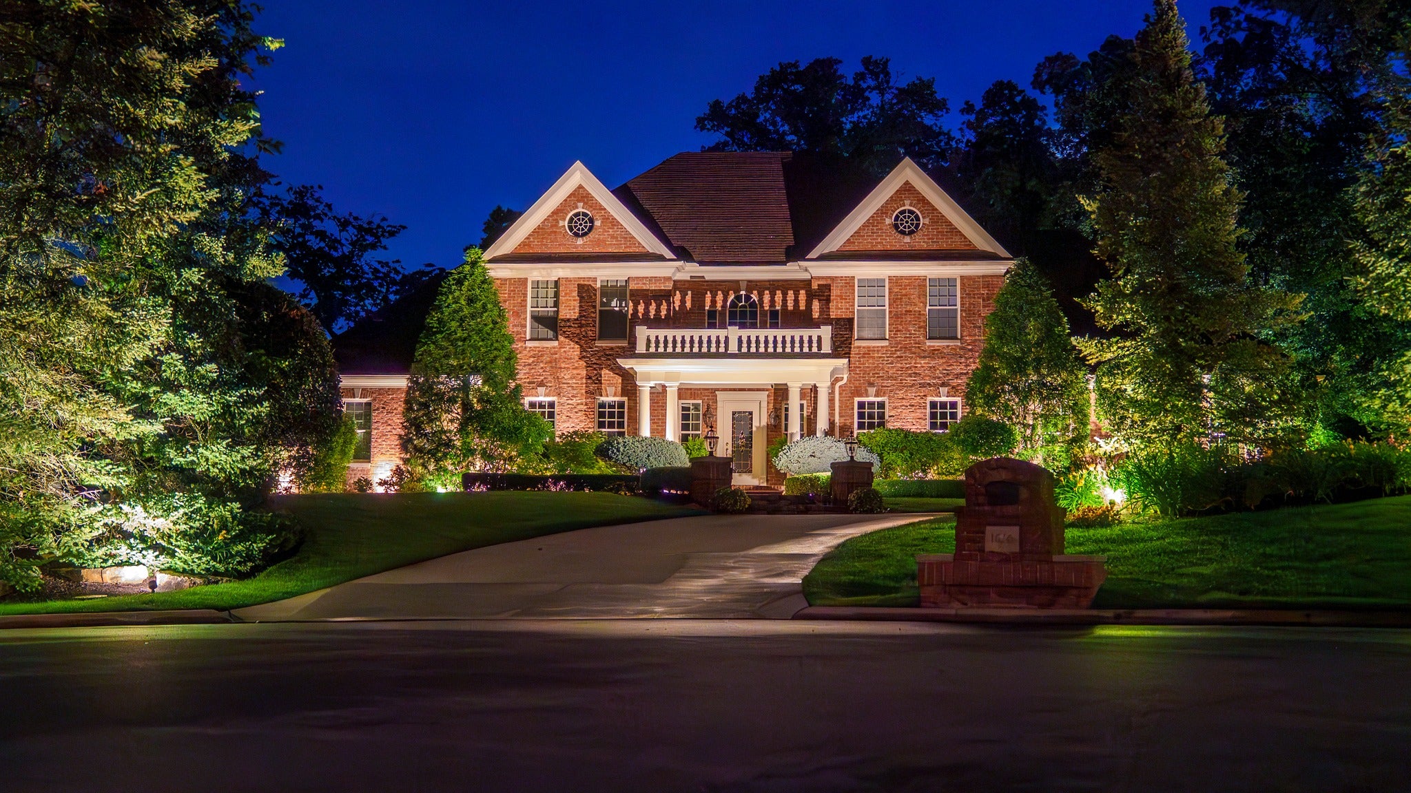 professional landscape lighting illuminating large brick estate home and front yard