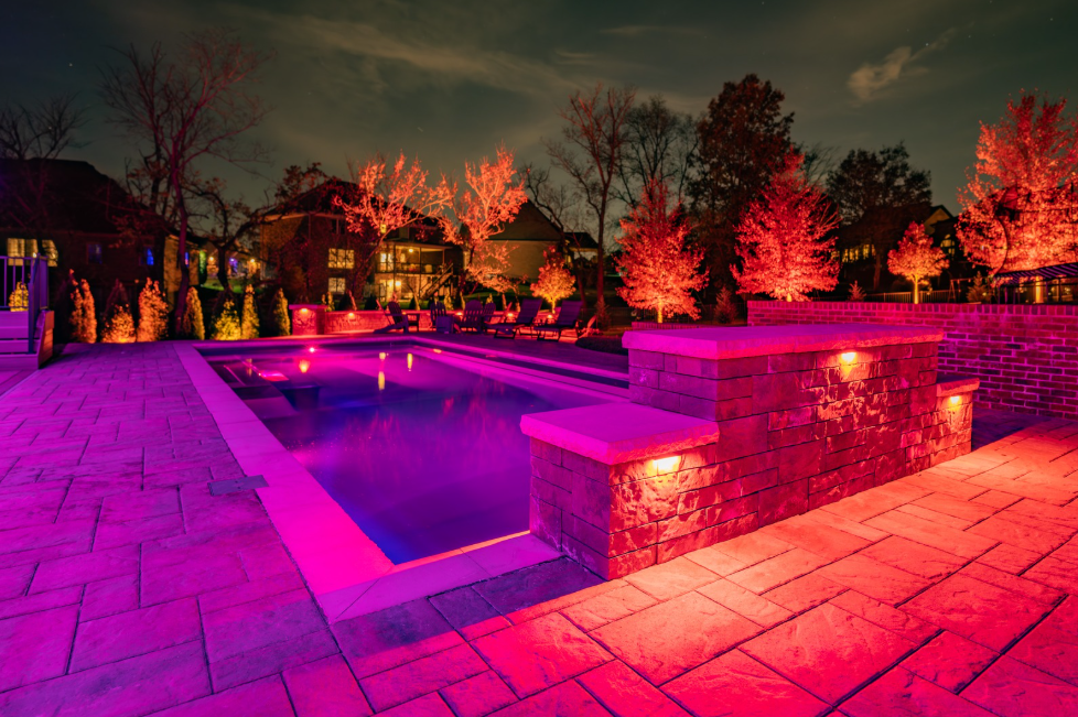 Outdoor lighting design illuminating a pool patio and surrounding landscape for nighttime backyard ambiance