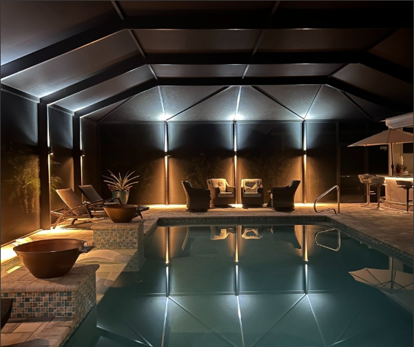 Professional pool and lanai lighting installation illuminating a screened pool enclosure and seating area at night